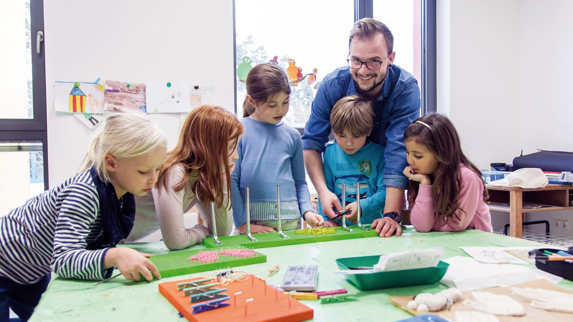 Ein junger Mann steht mit einer Kindergruppe an einem Tisch in einem großen Raum.