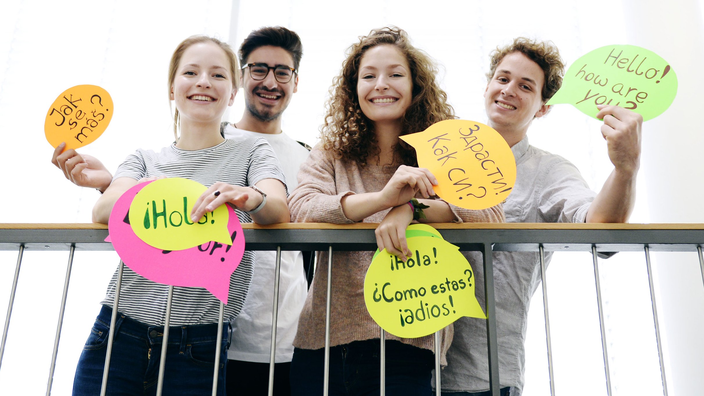 Four young people are showing colourful cards with greetings in different languages on them.