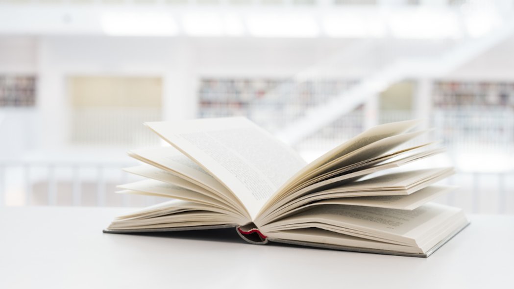 Auf einer hellen Oberfläche liegt ein aufgeschlagenes Buch.