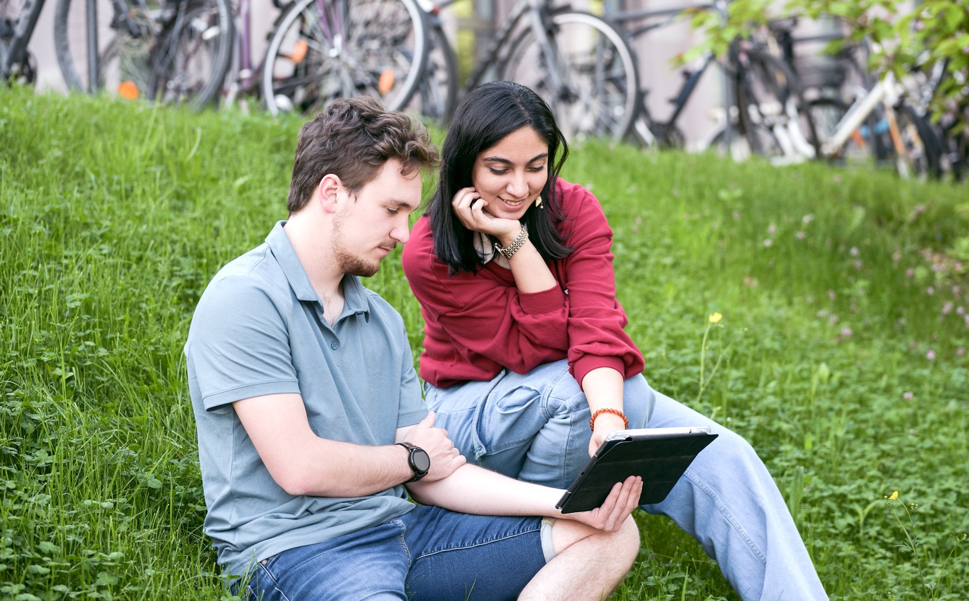 Eine Studentin und ein Student sitzen im grünen Gras mit Tablet.