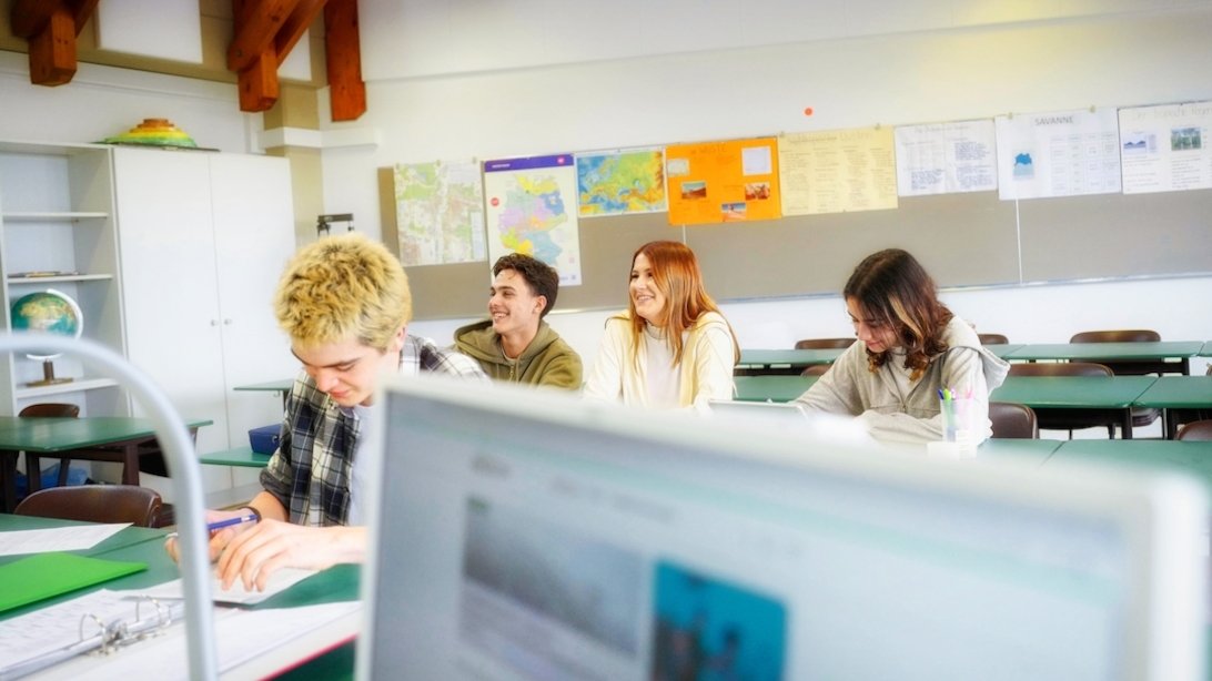 Zwei Schülerinnen und zwei Schüler sitzen in einem Unterrichtsraum und folgen dem Unterricht.