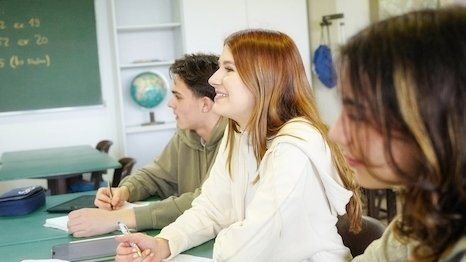 Zwei Schülerinnen und ein Schüler sitzen in einem Unterrichtsraum und arbeiten mit Tabletcomputern.