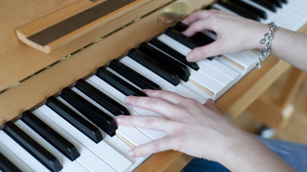 Ausschnitt auf die Tastatur eines Klaviers, auf welcher Frauenhände mit silbernem Armband einen Akkord spielen.