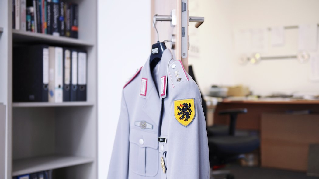 Blick auf eine graue Uniform der Bundeswehr, die an einem Türgriff hängt.