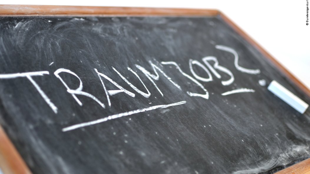 Auf einer schräg liegenden Schreibtafel mit Holzrand steht in Großbuchstaben das Wort "Traumjob" mit einem Fragezeichen dahinter. Unter dem Fragezeichen liegt ein Stück Kreide.