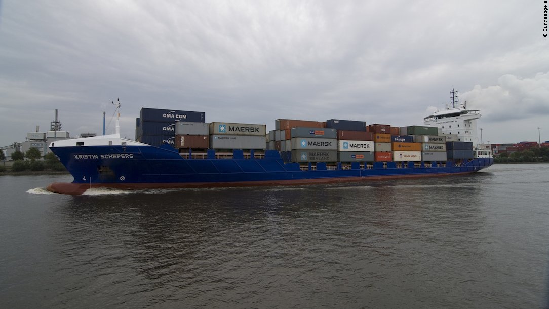 Ein Containerschiff fährt an der Küste entlang.