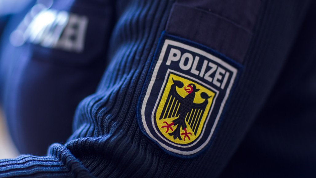 Nahaufnahme eines Polizeiwappens auf einem blauen Pullover am linken Oberarm einer Polizistin.