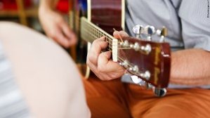 Detailansicht eines jungen Mannes, der auf einer Akustik-Gitarre spielt.
