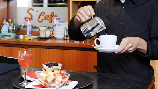 Barkeeper schenkt einen Kaffee aus einem Kännchen ein.