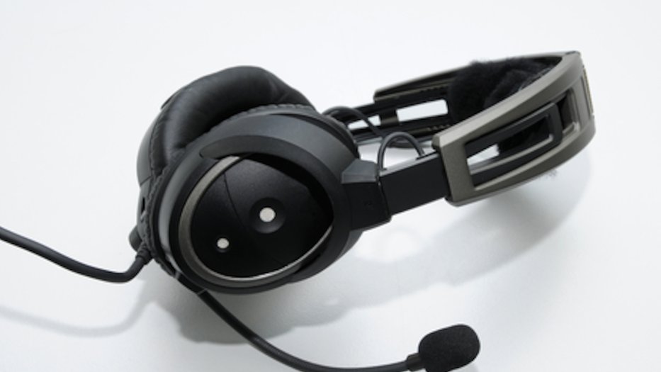 Ein kabelgebundenes schwarzes Headset mit Kopfbügeln, Ohrmuscheln und Mikrofon liegt auf einer hellen Oberfläche.