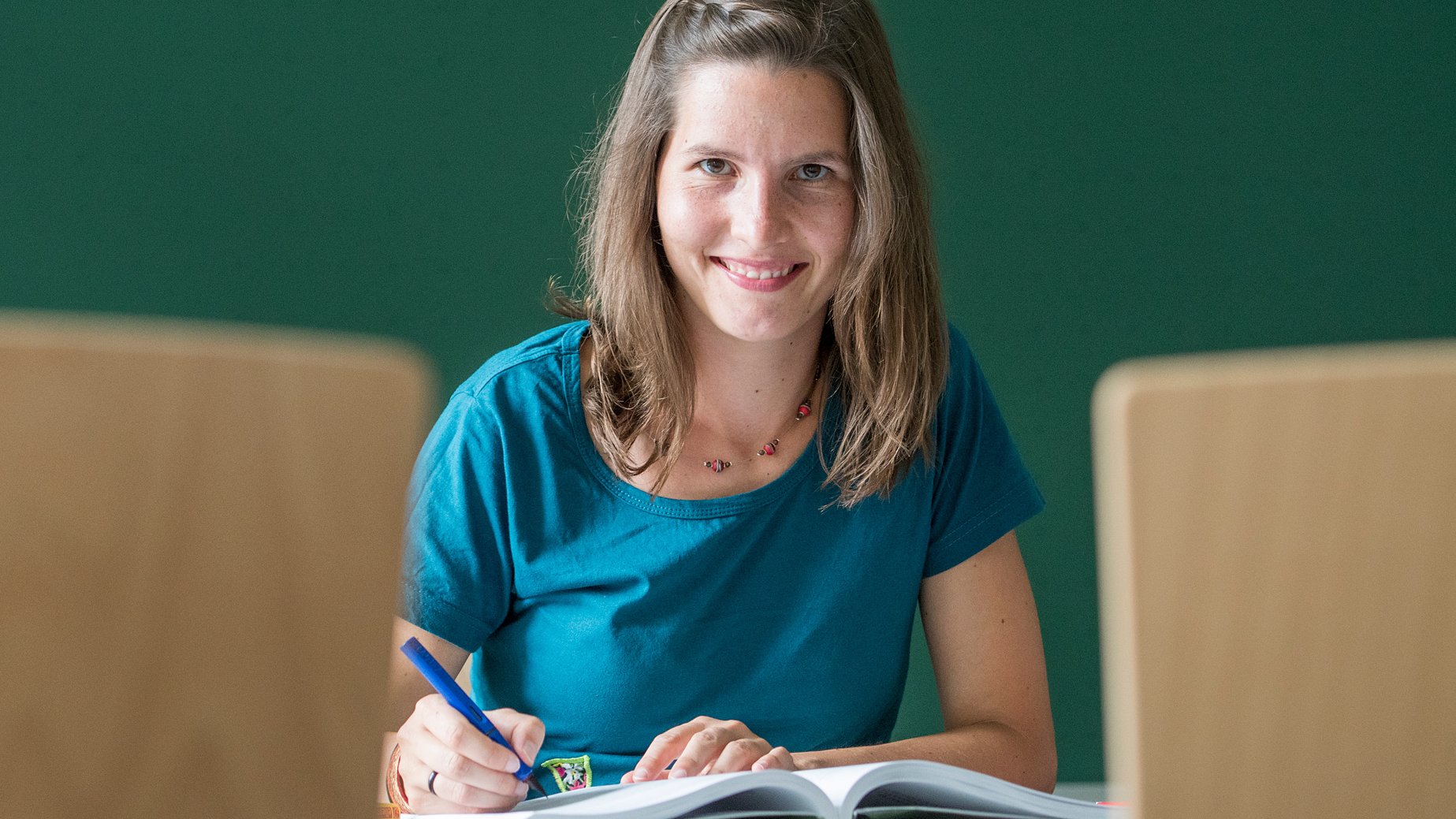 Eine junge Lehrerin sitzt vor einer Tafel und schreibt.