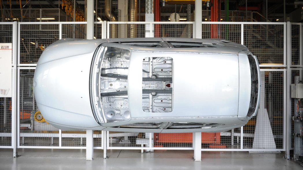 Die silberne Karosserie eines Automobils wurde zur Veranschaulichung mit dem Unterboden an ein Absperrgitter in einer Werkhalle montiert.