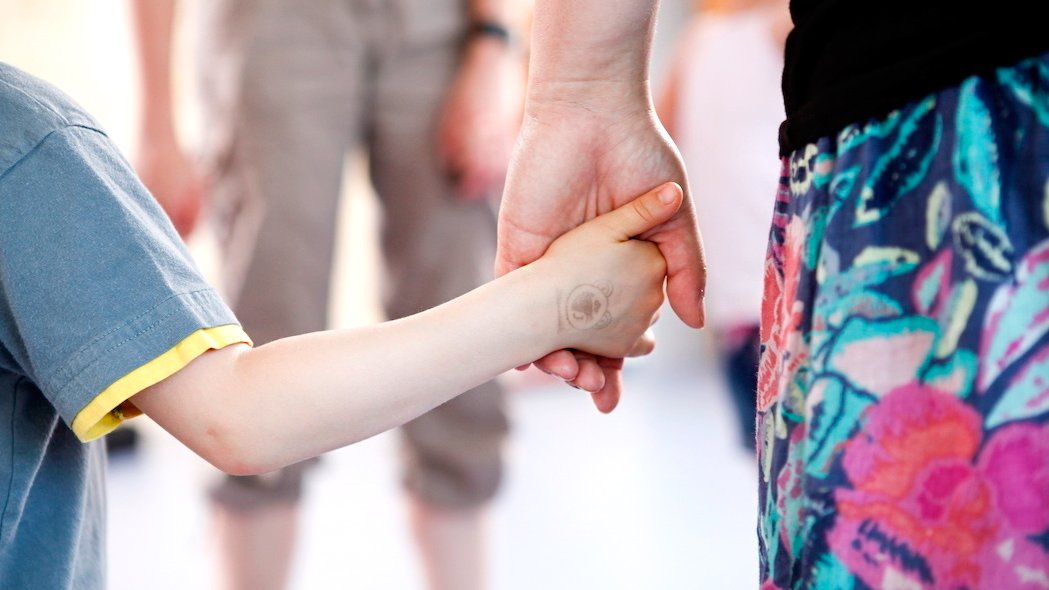 Nahaufnahme einer Frau, die ein Kind an der Hand führt.