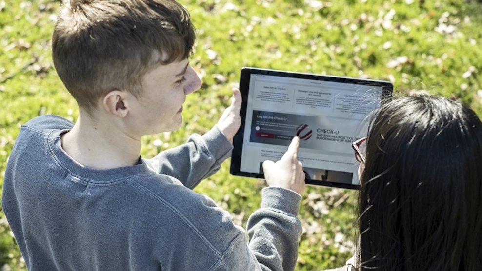 Ein junger Mann zeigt einer jungen Frau Check-U auf einem Tablet.