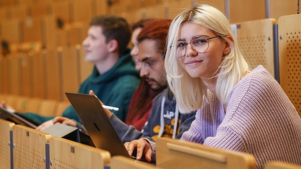 Zwei Studentinnen und zwei Studenten sitzen in einem Hörsaal und arbeiten mit Tablets und Laptops.