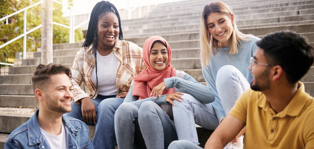 Eine Gruppe von jungen Frauen und Männern sitzen auf einer Treppe und unterhalten sich 