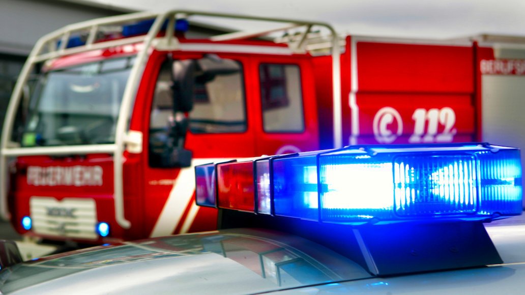 Detailaufnahme von einem Blaulicht auf einem Fahrzeugdach, welches leuchtet. Im Hintergrund erkennt man ein großes rotes Löschgruppenfahrzeug.
