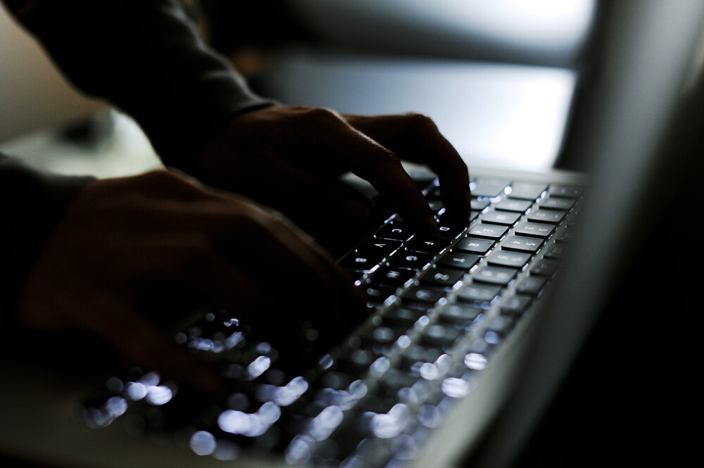 Zwei Hände tippen in dunkler Umgebung auf einer schwarzen Tastatur.